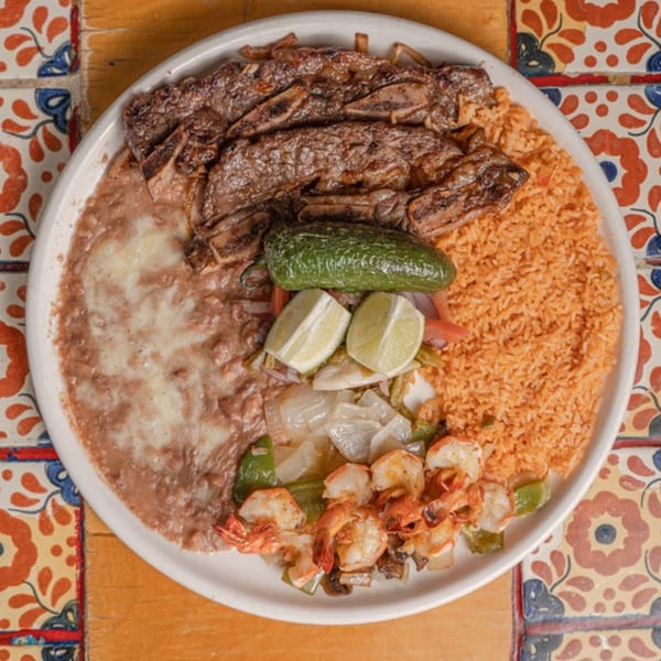 A Mexican platter with grilled ribs, refried beans, rice, shrimp, and a jalapeño.