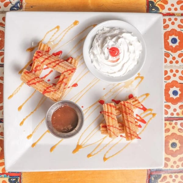 Don Pedro Mexican Restaurant's churros dessert with whipped cream, cherry, and caramel drizzle on a white plate.